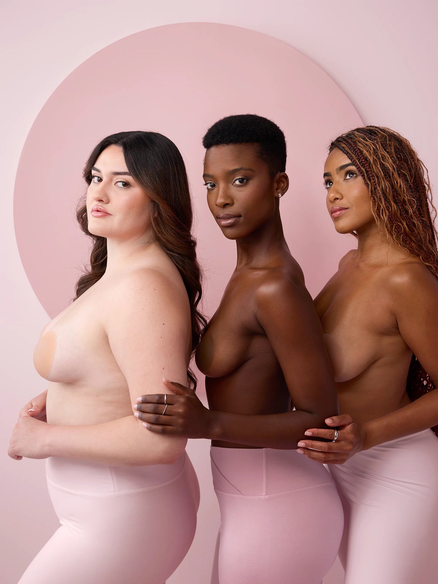Three women of different ethnicities standing back-to-back against a pink background